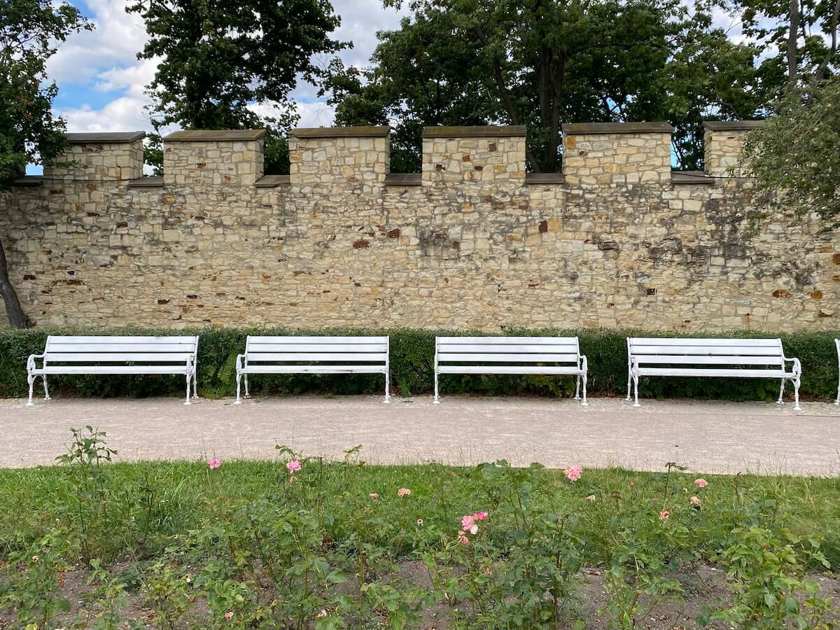 White benches in Petrin park with Hunger Wall behind them